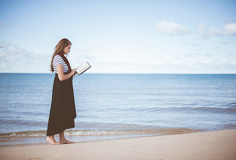 Frau betet mit Bibel in der Hand am Strand