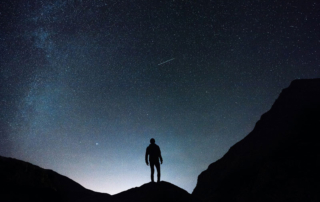 Man standing on a mountain top gazing at the starry sky
