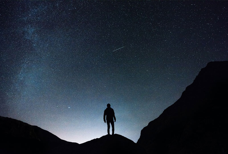 Man standing on the top of a mountain and looking at the starry sky